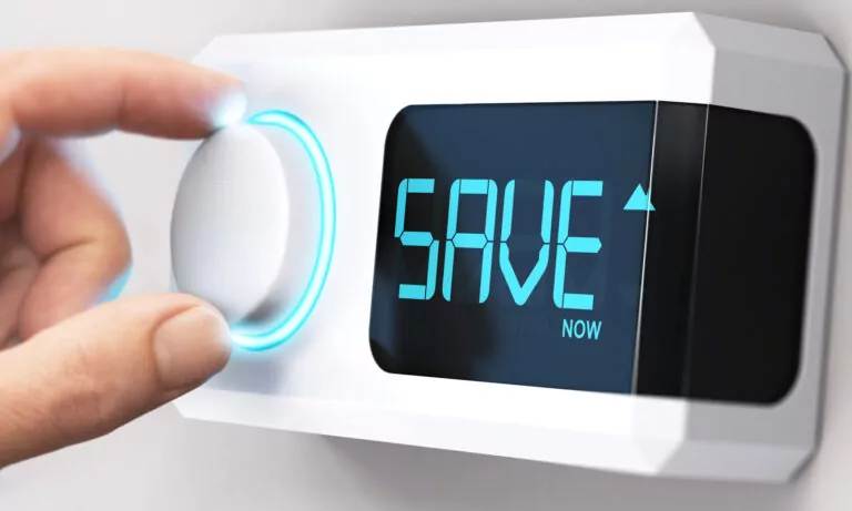 Hand turning a thermostat knob to increase savings by decreasing energy consumption