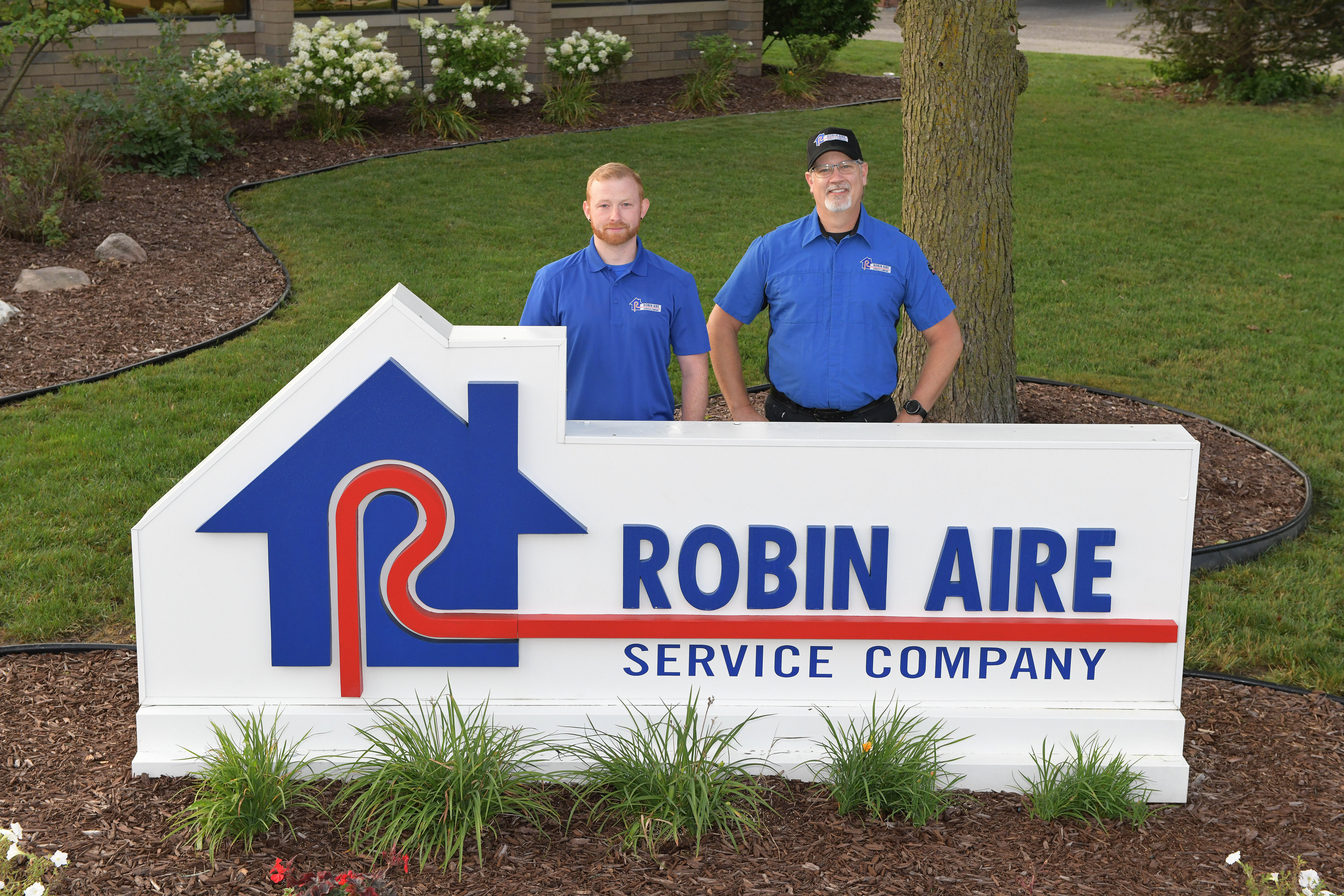 Two Robin Aire employees standing behind a Robin Aire sign
