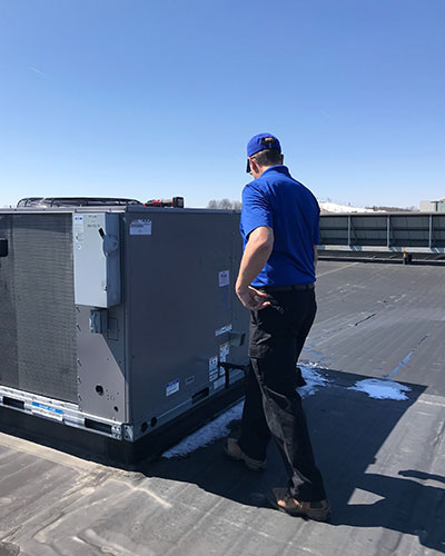 A Robin Aire technician observing a commercial AC unit on a rooftop