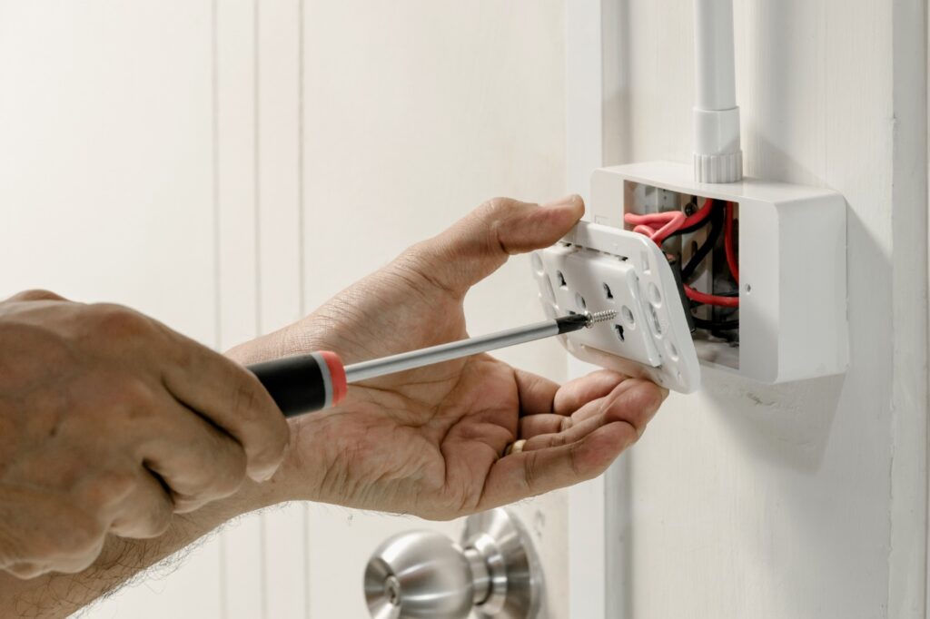 Hands with a screwdriver installing an outlet in someone’s home 