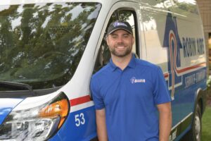 Robin Aire technician in blue polo shirt and baseball cap standing in front of an Robin Aire truck. 