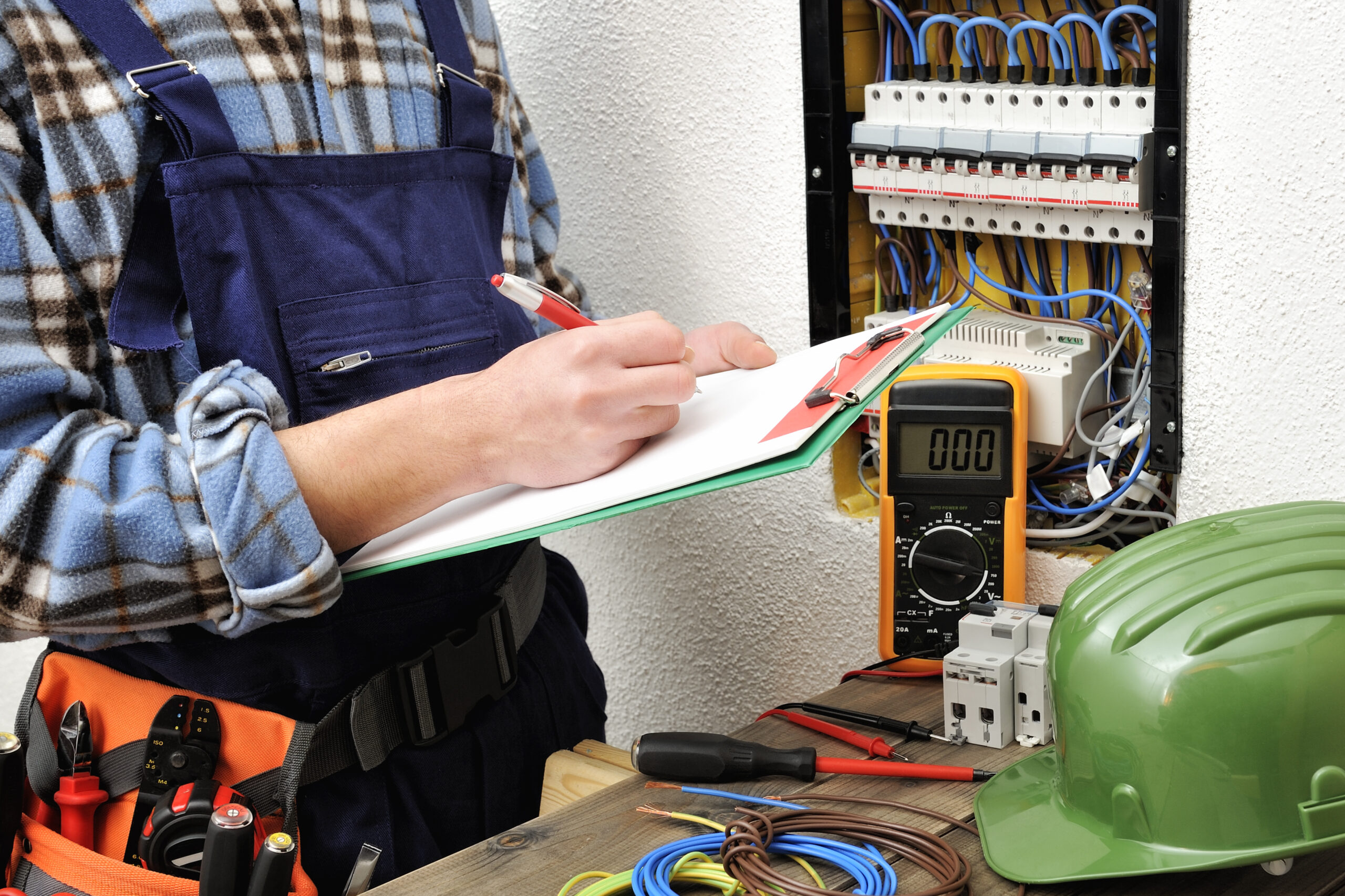 Electrician with a clipboard standing next to an electrical panel